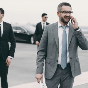 smiling-businessman-walking-with-bodyguards-and-talking-by-smartphone.jpg